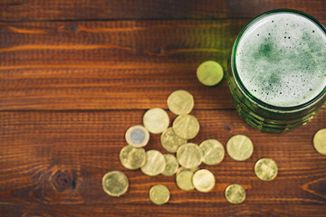 Beautiful background for St. Patrick's day with a glass of green beer and gold coins on a wooden table. Free space