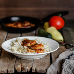 Fish in tomato sauce and pasta in a white plate on a wooden surface (on a table) and vegetables