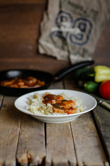Fish in tomato sauce and pasta in a white plate on a wooden surface (on a table) and vegetables