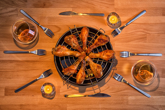 Fried chicken legs on the round mesch among the forks, candles and glasses with cognac 