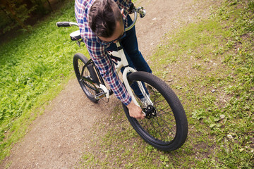 Fototapeta na wymiar Trendy man repairing bicycle wheel at park