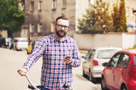 Young trendy man holding bike handlebar and mobile