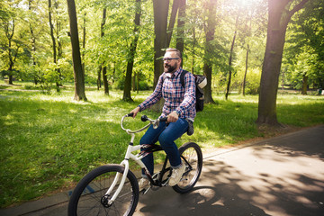 Fototapeta premium Trendy hipster man riding bicycle through park