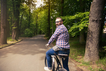 Young modern man riding bike looking back in park