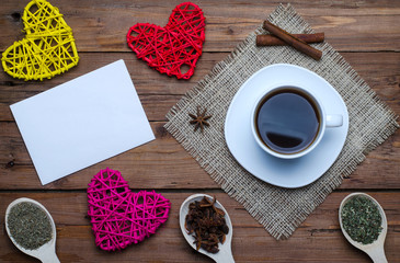 A cup of hot coffee and a blank sheet of paper on a wooden background, top view.