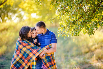 happy family with the little daughter walks in the evening park on a sunset, embrace and take cover a warm plet