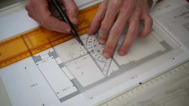 Architect drawing blueprints plan, graph, design, geometric shapes by pencil on large sheet of Tracing paper at office desk. Engineer hands, Working with triangle ruler and pencil