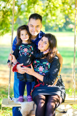 happy family with the little daughter walks in the evening park on a sunset, ride a swing and embrace