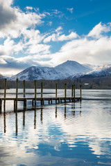 A pier reflected in Lake Derwent  with snow covered mountains in the English Lake District