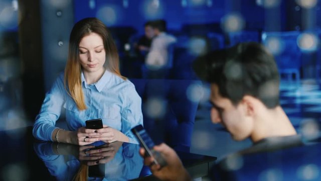 A couple in a cafe uses smartphones, ignoring each other. Lack of live communication