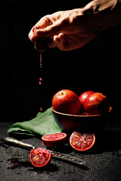 hand squize out juice from qurater of blood orange on dark background