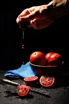 hand squize out juice from qurater of blood orange on dark background