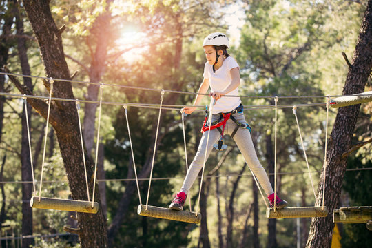 Happy school girl enjoying activity in a climbing adventure park on a summer day