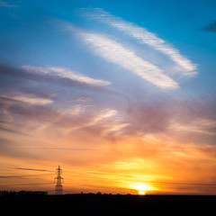 Sunset and electricity pylon. A dramatic sky and sunset scene in rural England with the silhouette of a UK National Grid electricity pylon.