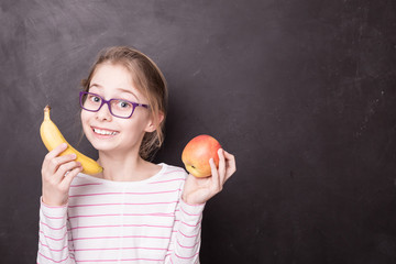 Happy chid girl with apple and banana at the chalkboard