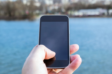 man holding a cell phone with the river in the background