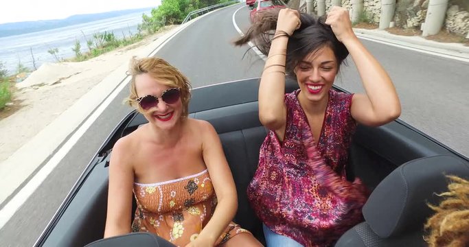 Two beautiful young women raising their arms up while riding in convertible