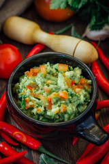 Guacamole dip with ingredietns in black ceramic bowl.