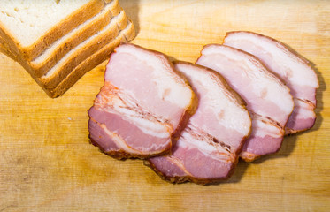Raw smoked bacon slices with bread on wooden board