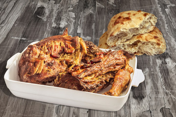 Roasted Lamb Shoulder in Porcelain Casserole with Pitta Bread Halves Set on Old Weathered Cracked Wooden Table Surface
