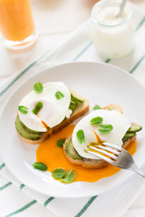 Vegetarian breakfast: avocado toast with poached eggs, orange juice, yogurt and jam on white wooden background. Selective focus