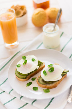 Vegetarian breakfast: avocado toast with poached eggs, orange juice, yogurt and jam on white wooden background. Selective focus