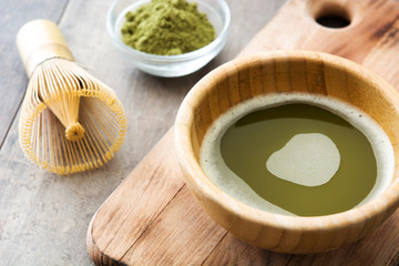 Matcha green tea in a bowl and bamboo whisk, on wooden background
