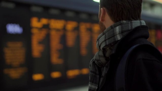 Young professional male looks at departure board and tickets