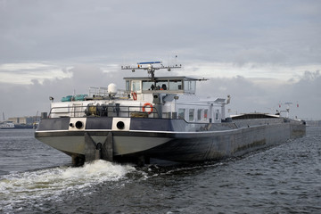 Cargo barge, seen on the back, sailing on a river © hoeks