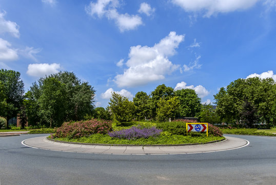 Small roundabout with plants, trees and traffic sign without any traffic, against a beautiful blue sky
