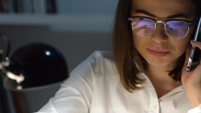 Smiling happy business woman talking on mobile phone while workig with documents in office