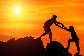 Silhouette man pulled up woman to the mountain at sky sunset.