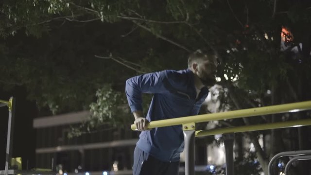 Young bearded man doing exercises on parallel bars at sports playground 