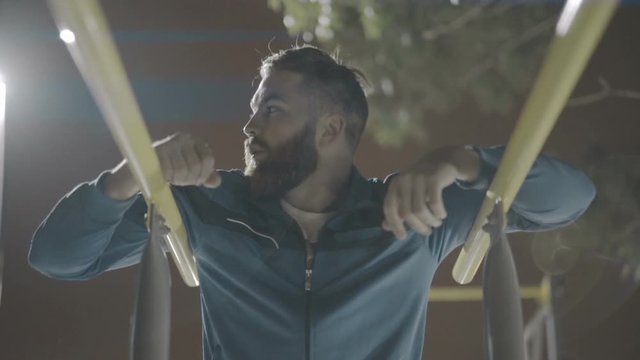 Tired young sports man resting after workout on parallel bars at a sports playground 