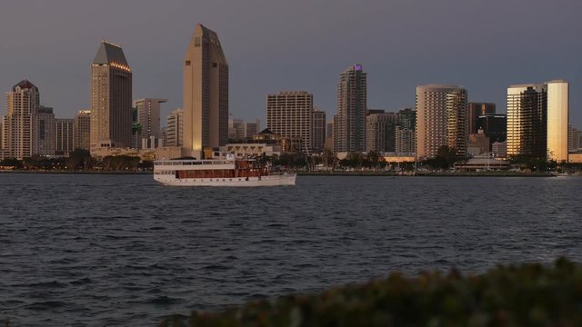 A picturesque establishing shot of the San Diego skyline at dusk with a tour boat passing by in the bay.