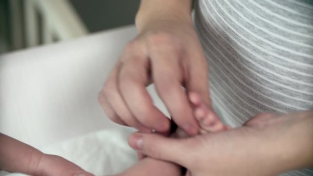 newborn baby caukasian etnicity with diaper mom hands foot massage her
