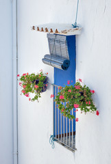 Mediterranean window. White facade: window with blue shutters and flowers on both sides