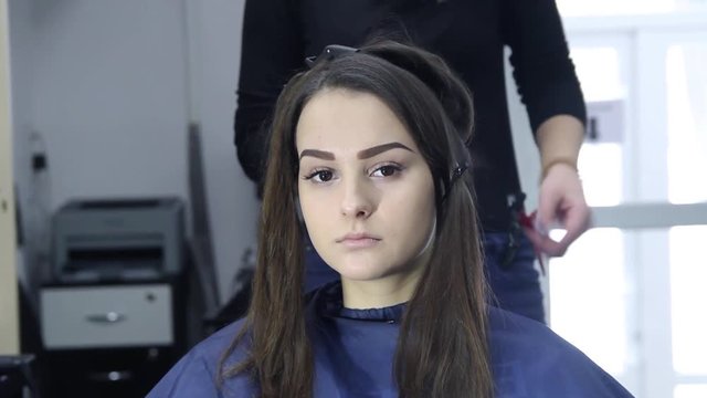 Female hairdresser standing and making hairstyle to cute lovely young woman in beauty salon