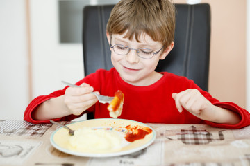 Adorable little school boy eating potato mash and chicken breast indoor