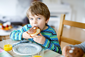 Adorable little preschool boy eating donut indoor