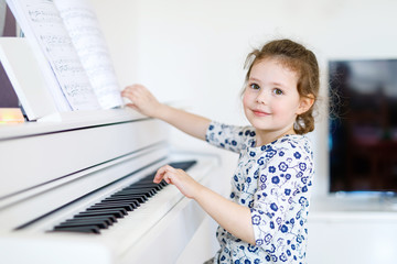 Beautiful little kid girl playing piano in living room or music school