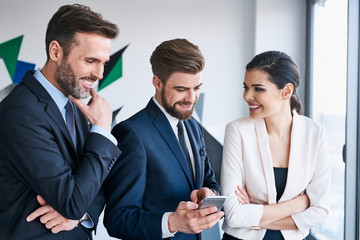 Group of business executives talking during coffe break at office sharing something on smartphone