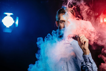 Young guy with a beard vaping and releases a cloud of vapor. hipster vaper smoke vaporizer.