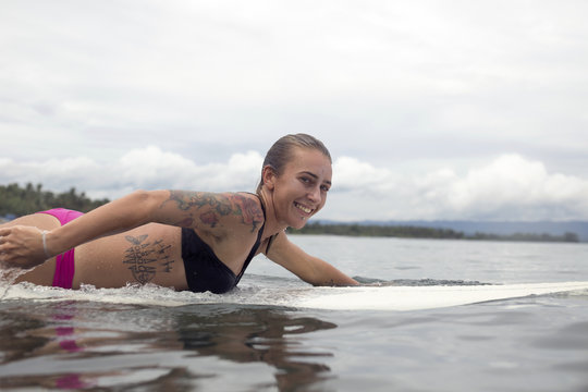 Indonesia, Java, smiling woman lying on surfboard on the sea