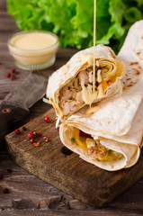 Shawarma chicken roll in a pita with fresh vegetables and cream sauce on wooden background....