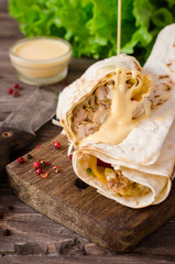 Shawarma chicken roll in a pita with fresh vegetables and cream sauce on wooden background. Selective focus