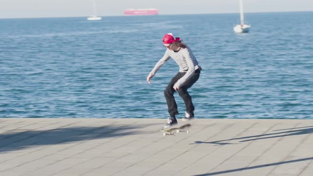 CLOSE UP: Pro skateboarder skateboarding and jumping 180 ollie, shov-it and kickflip trick along the ocean coast on sunny day. Cool skater jumping ollies and flips along the concrete shore at seaside
