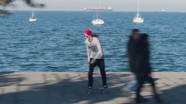 CLOSE UP: Young pro skateboarder performing 360 flip trick, cruising on sunny day with ocean in the background. Skater skateboarding and jumping along the coast at seaside on stunning summer day