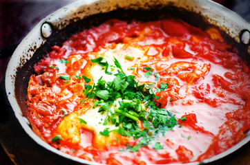 Shakshuka. Traditional jewish food and middle eastern cuisine recipe. Fried eggs, tomatoes, bell pepper and parsley in a pan. Close up, selective focus. Homemade breakfast