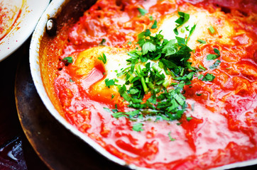 Shakshuka. Traditional jewish food and middle eastern cuisine recipe. Fried eggs, tomatoes, bell pepper and parsley in a pan. Close up, selective focus. Homemade breakfast
